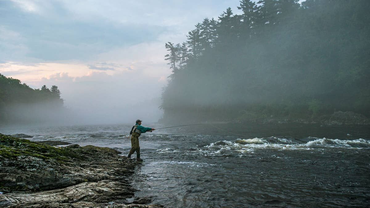 A fly angler casting into a misty river